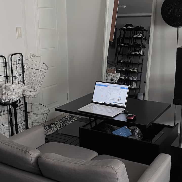 Modern living room in black and white tones featuring a two-seater sofa, a desk with a laptop, storage shelves, and a floor lamp