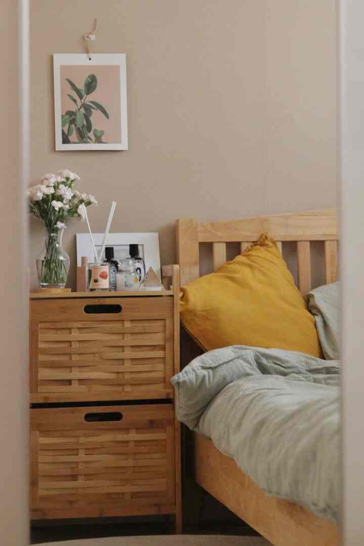 Beige-toned wall and natural wood furniture in a cozy bedroom featuring a mustard cushion and fresh flowers creating a warm atmosphere