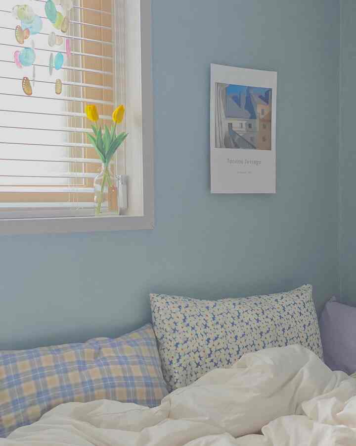 A bedroom with light blue walls and white duvet cover, featuring checkered and floral pillows creating a cozy atmosphere