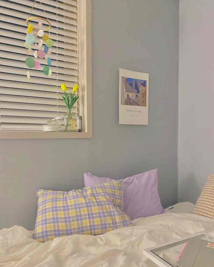 Cozy bedroom with gray walls, white duvet cover, and pastel-colored pillows arranged on the bed