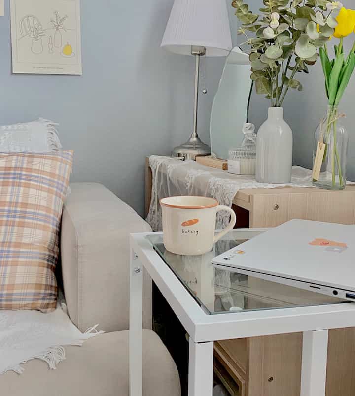 Natural-toned bedroom corner with beige sofa, side table featuring mug and laptop, creating a cozy atmosphere