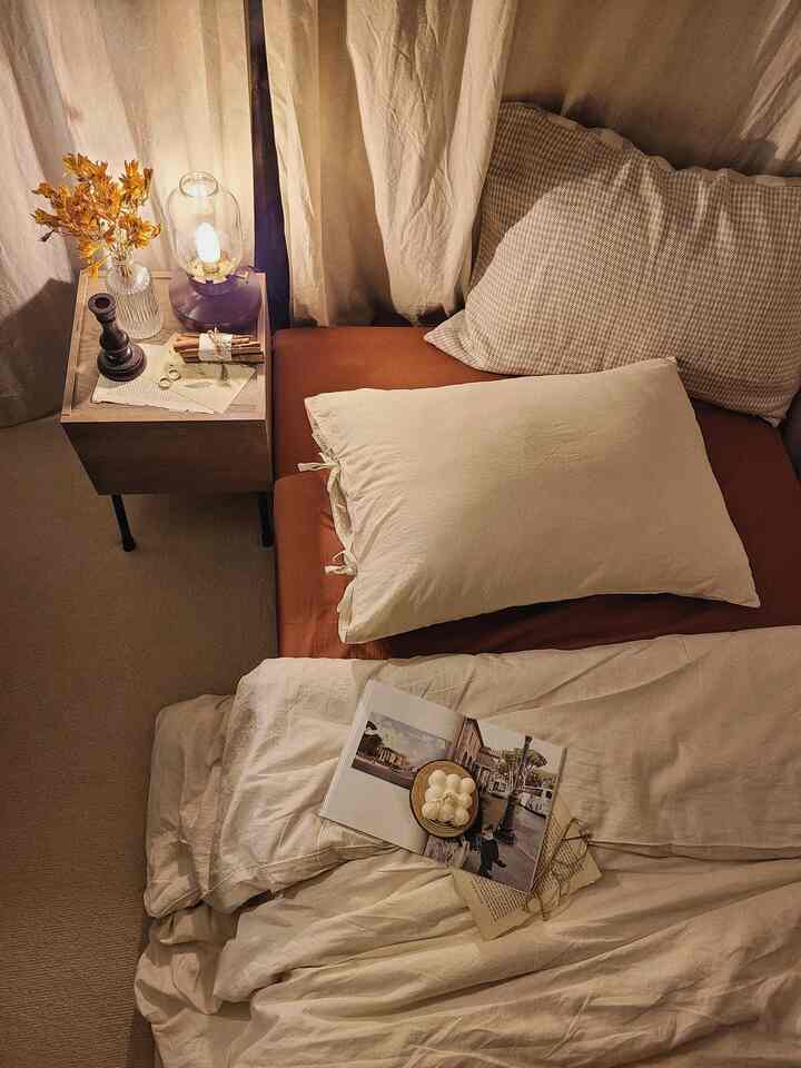 ベージュとナチュラルトーンのワンルーム寝室、ベッドとナイトテーブル、温かみのある照明が配置された印象的な空間