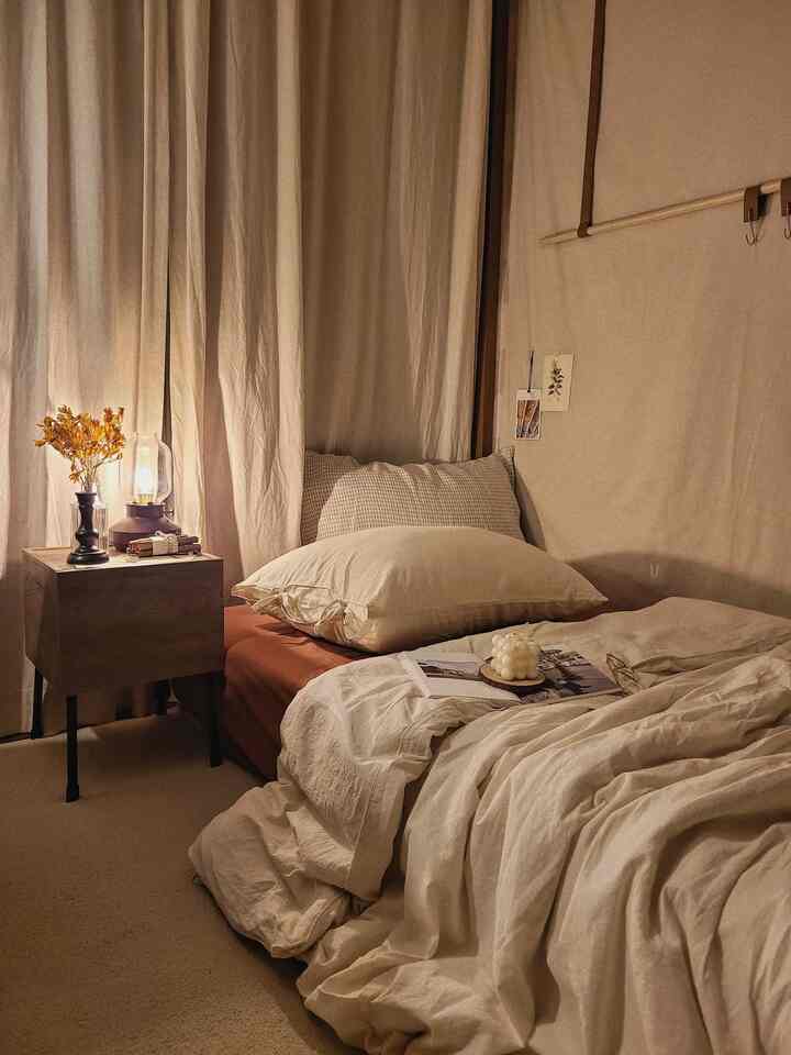 暖かいベージュと木目調のワンルーム寝室、居心地の良い掛け布団カバーとナイトテーブルランプが配置された雰囲気のあるインテリア