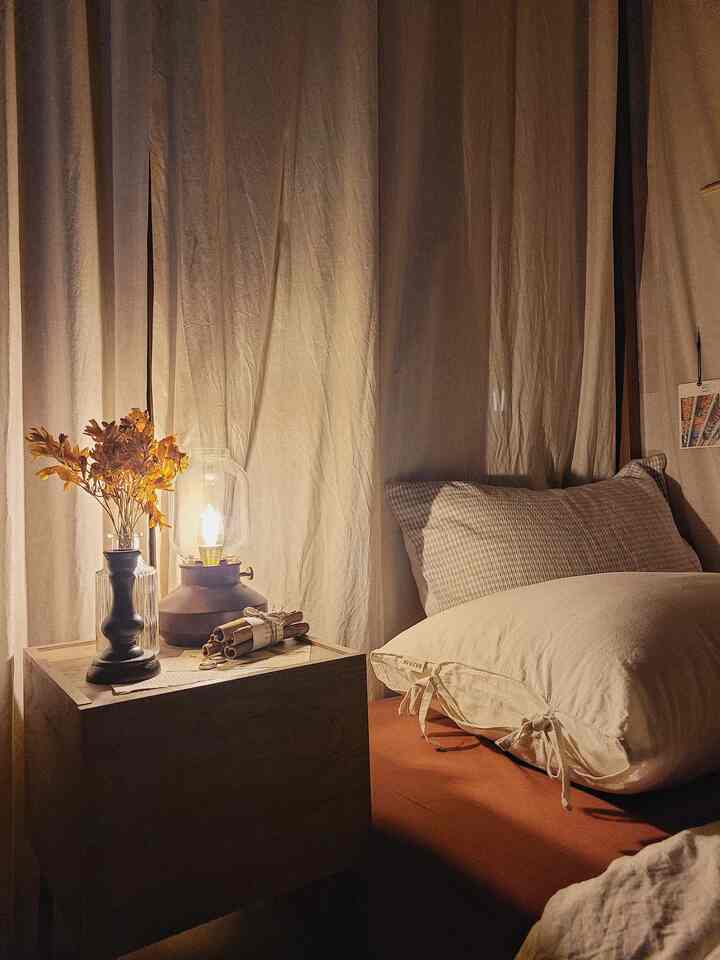 ベージュのカーテンとブラウンのベッドシーツが調和するワンルーム寝室、ヴィンテージ照明と居心地の良い秋の小物が配置された雰囲気のあるインテリア