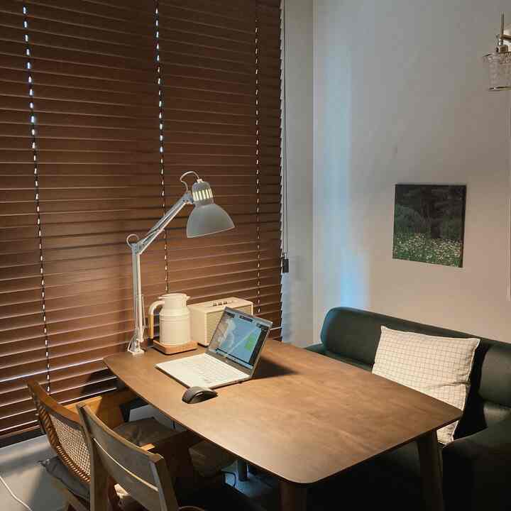 Wood tone and dark green accented home office space for two, featuring wooden blinds and dining table creating a cozy atmosphere