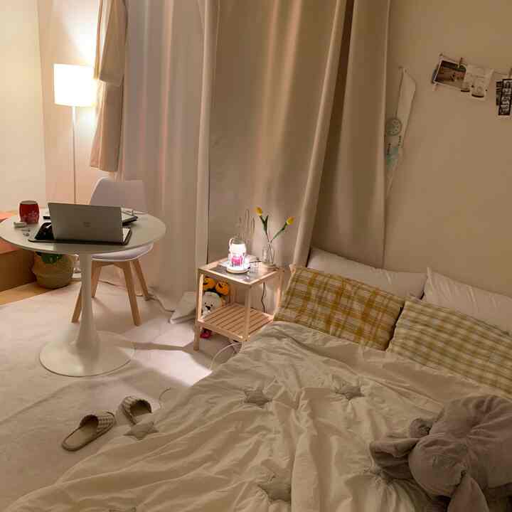 ベージュと白を基調としたワンルームの寝室、木製のナイトテーブルと丸いカフェテーブルが配置された居心地の良いナチュラルなインテリア