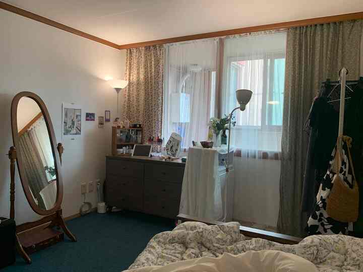 Vintage-style bedroom corner featuring floral fabric curtains, wooden vanity, and large wooden standing mirror with cozy atmosphere