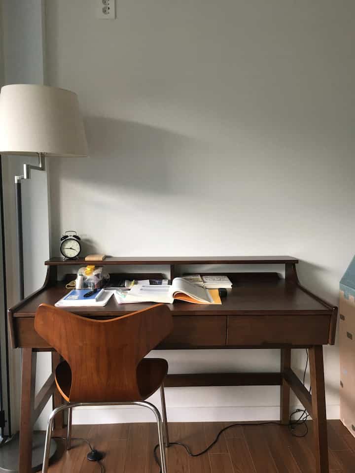 Natural wood tone living room corner next to veranda featuring desk, chair, and floor lamp with cozy home office atmosphere