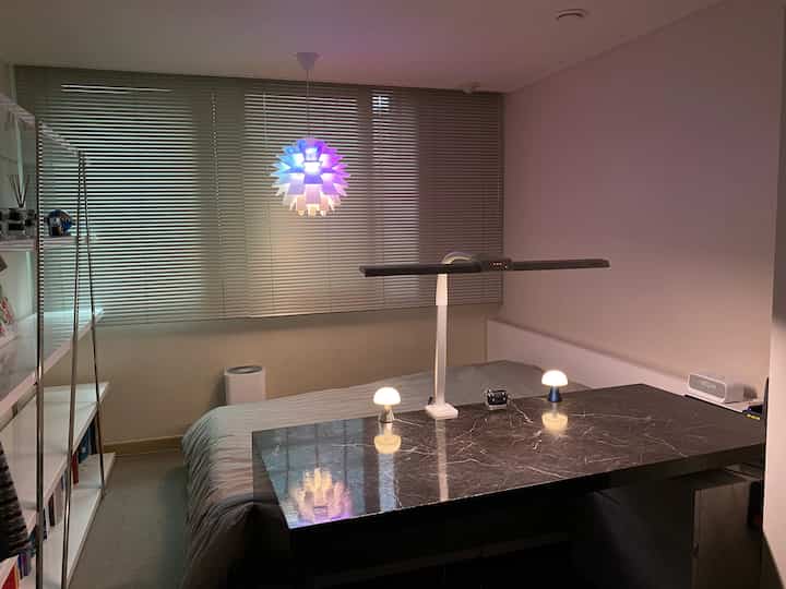Modern studio bedroom in gray and white tones featuring a large black marble desk and pendant light