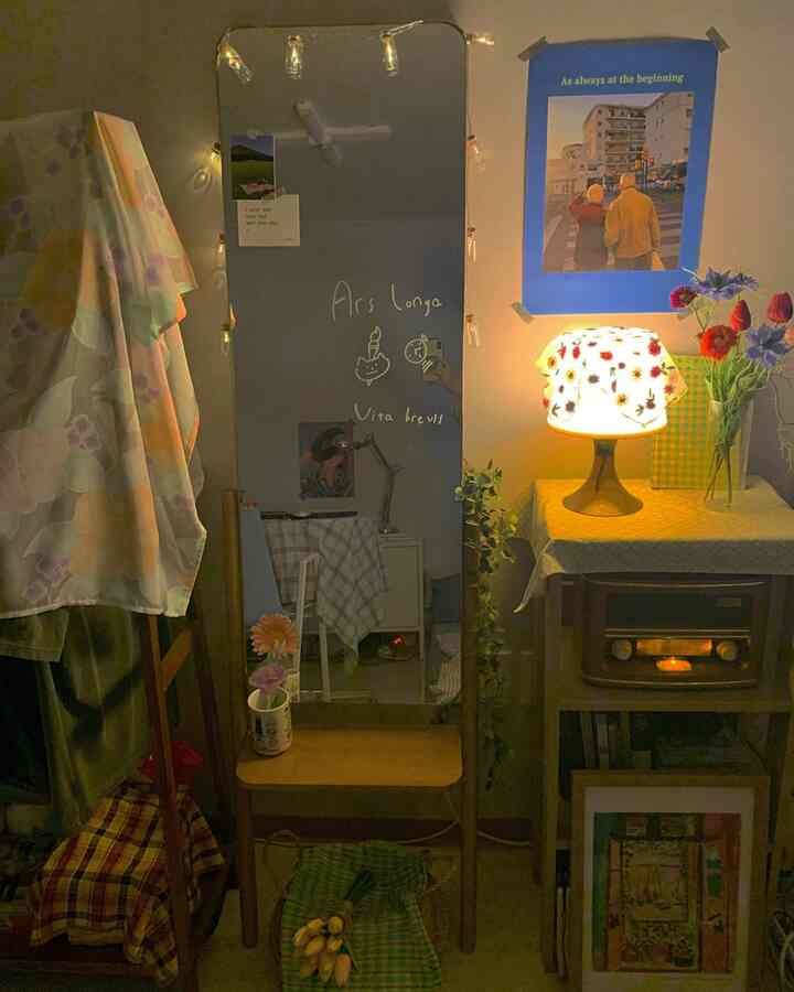 温かみのある照明と木製家具、ポスターと全身鏡が配置された居心地の良いワンルームインテリア