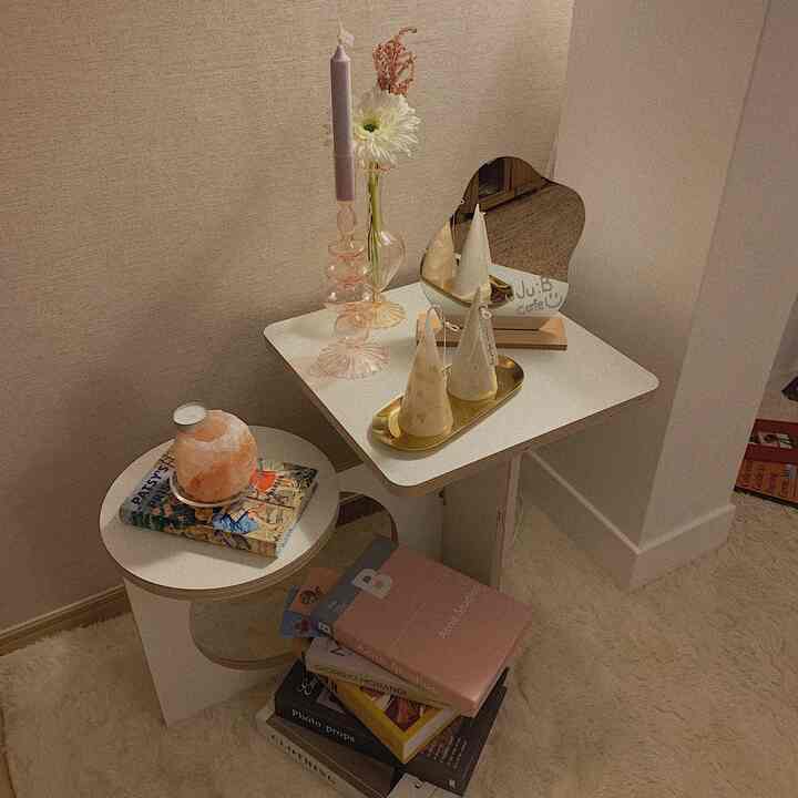 ベージュの壁とナチュラルカラーのラグ、サイドテーブルにキャンドルや鏡、装飾用の本が置かれた印象的なコーナースペース