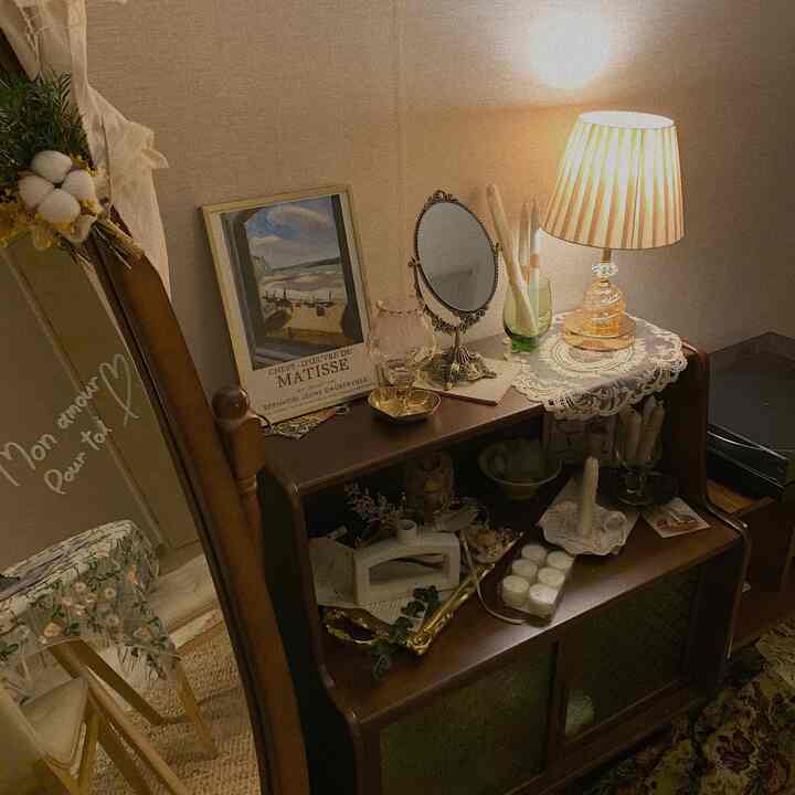 暖かい木目調とヴィンテージスタイルのナイトテーブルにキャンドルや額縁、柔らかい照明が配置された雰囲気のあるインテリア