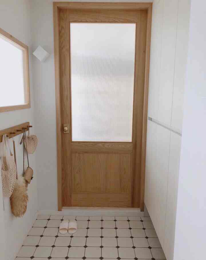 Bright white and wood tone entrance space featuring a wooden interior door and built-in shoe cabinet, presenting a clean and warm atmosphere