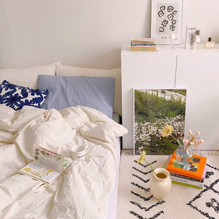 White and blue toned studio apartment bedroom featuring bed, cabinet, and posters with a cozy natural atmosphere