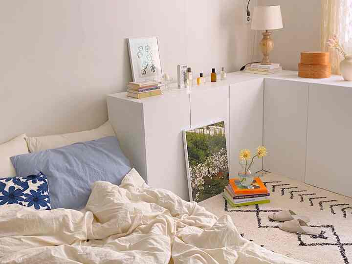 A white and beige toned studio bedroom featuring a neat cabinet, rug, and cozy bedding with a calm atmosphere