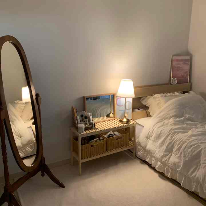 Cozy bedroom with natural wood tones and white hues featuring a full-length mirror and table lamp in a compact space