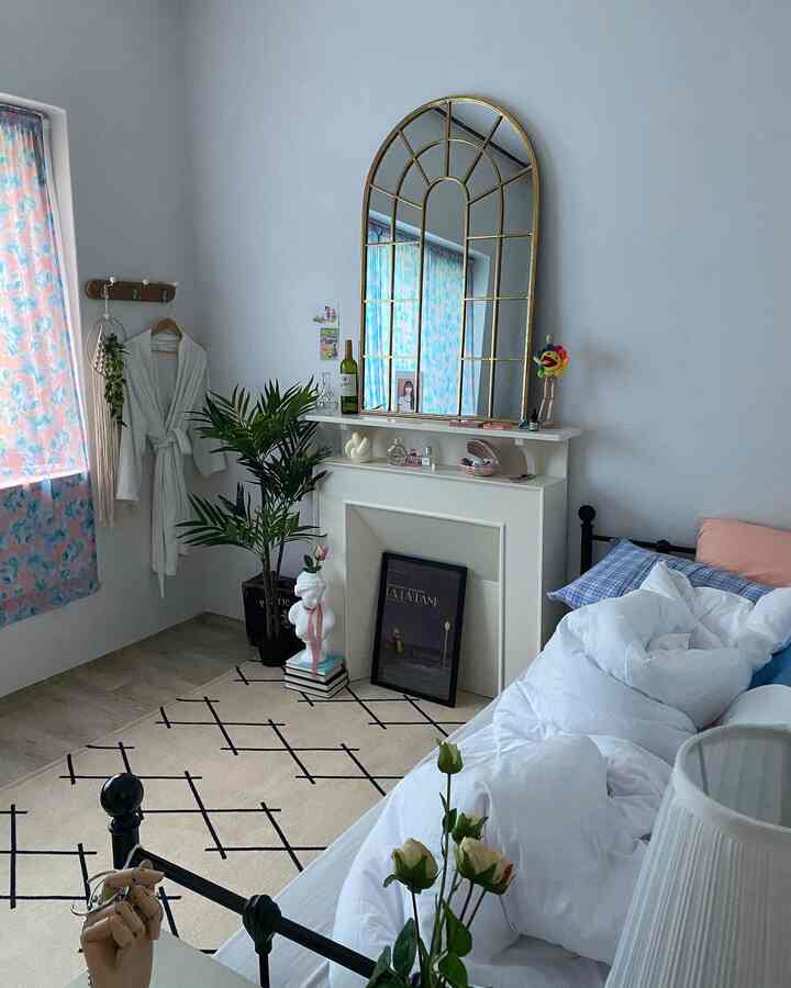 White-toned bedroom with patterned curtains, a fireplace, large arched mirror, and bed creating a clean, natural atmosphere