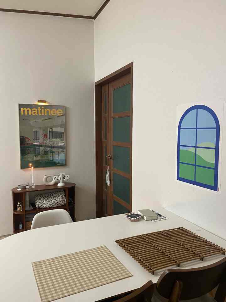 Dining room with white walls and brown wooden furniture, featuring a central white table with placemats, posters, and a candle creating a cozy atmosphere