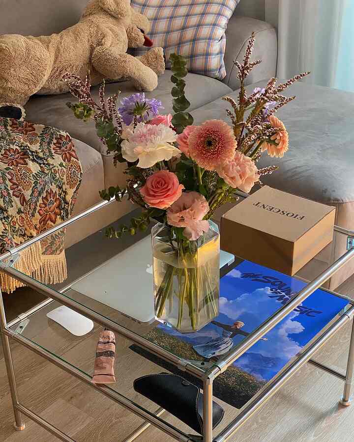Light gray toned living room featuring a glass coffee table with fresh flowers and a beige dog plush, creating a cozy atmosphere