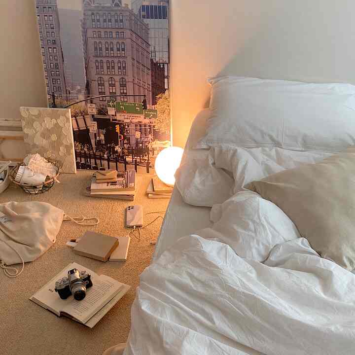 Cozy bedroom in warm natural tones featuring white bedding, beige rug, large cityscape poster, and spherical lamp