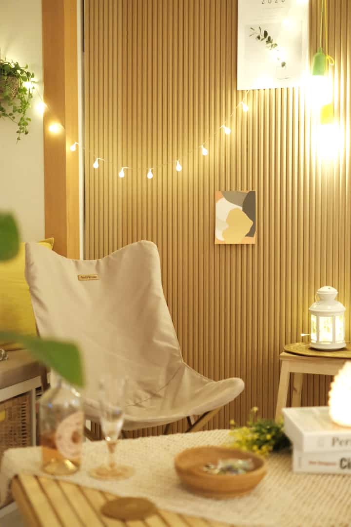 ウッドトーンの壁パネルとベージュのキャンプチェア、ストリングライトが調和した快適なホームキャンピングリビング