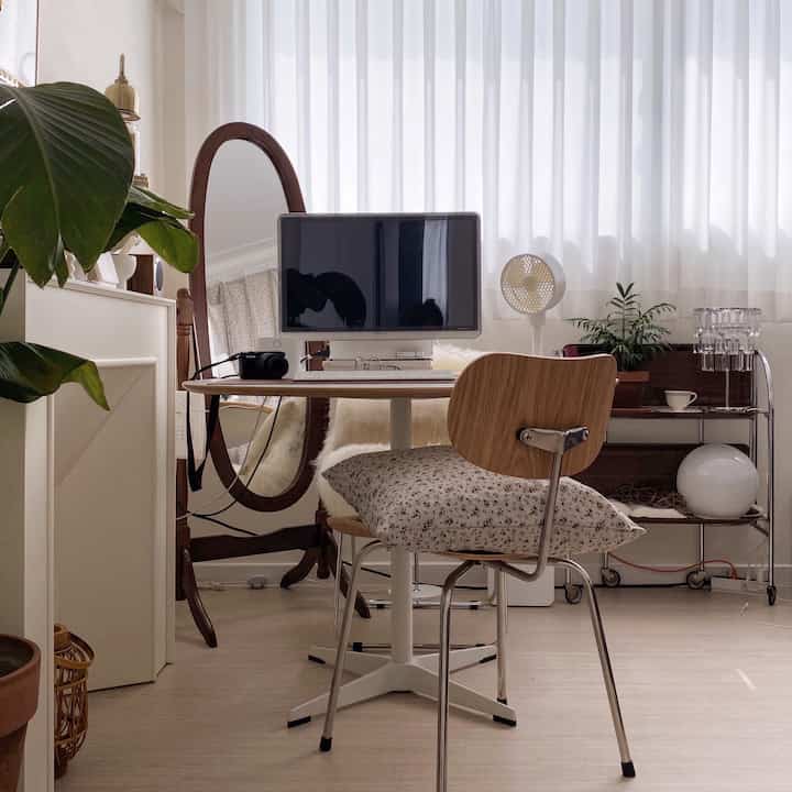 白と木目調が調和した寝室の一角にあるホームオフィス、丸テーブルとヴィンテージトロリーが配置された温かみのある雰囲気のインテリア