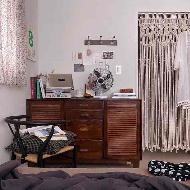 白と木目調が調和したヴィンテージ風寝室、木製キャビネットとマクラメカーテンが温かみのある雰囲気を演出。