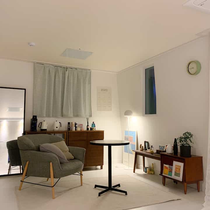 ナチュラルモダンな色調のリビング、グレーのアームチェアと丸テーブル、木製家具が配置された落ち着いた空間