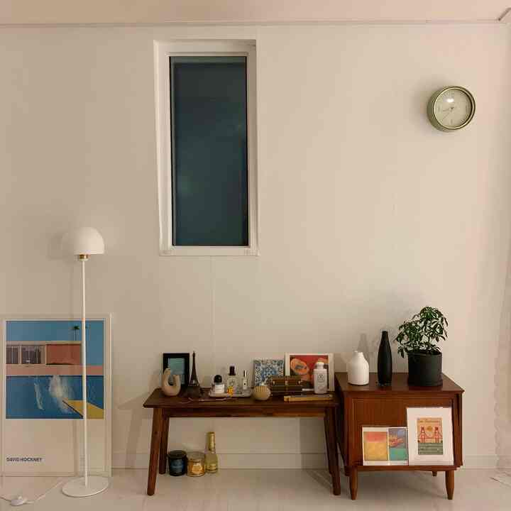 White and brown toned living room featuring simple natural style with a wall clock, floor lamp, vases, and plant arranged neatly
