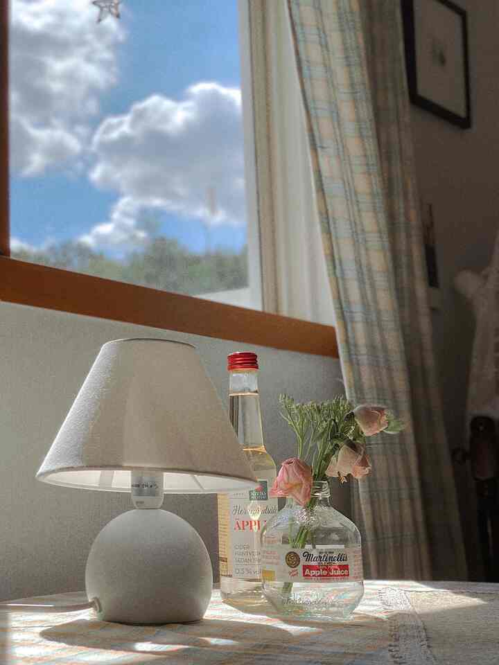 ラベンダーとベージュの柔らかなトーンのカーテンがある陽射しの良いおうちカフェ空間、テーブルクロスとフロアランプが温かみのある雰囲気を演出