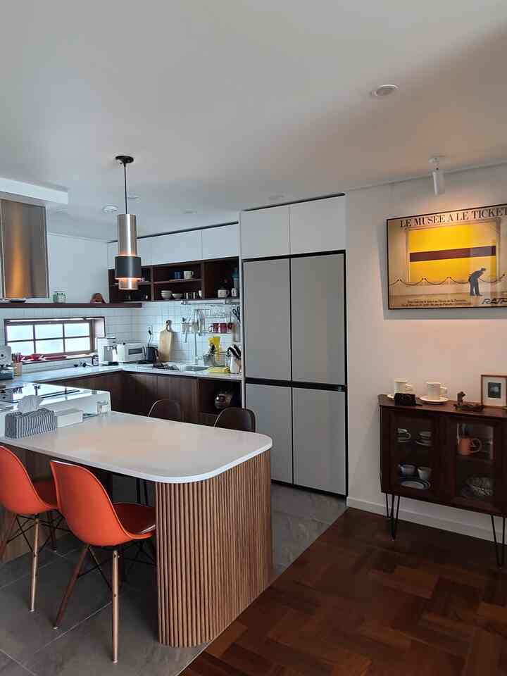 白と茶色のトーンのキッチン、オレンジのダイニングチェアが配置されたモダンで清潔感のある空間