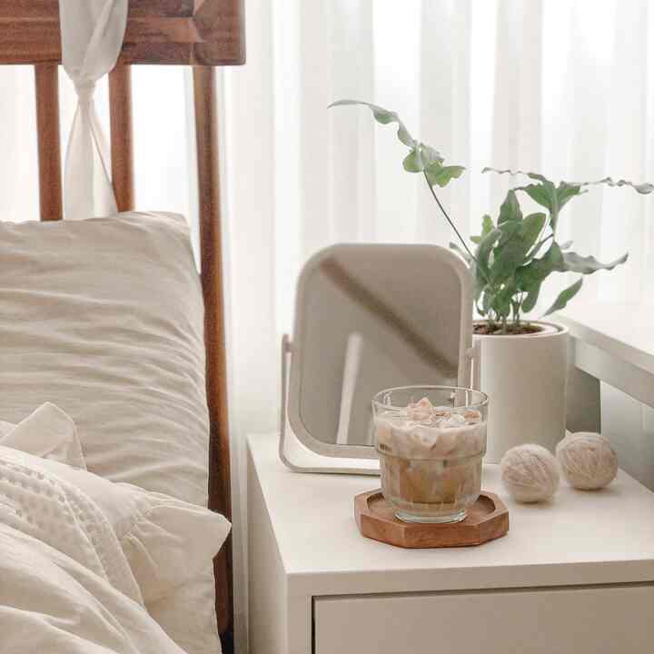 White and wood tone bedroom featuring a bed frame, plant pot, and tabletop mirror with a cozy modern atmosphere
