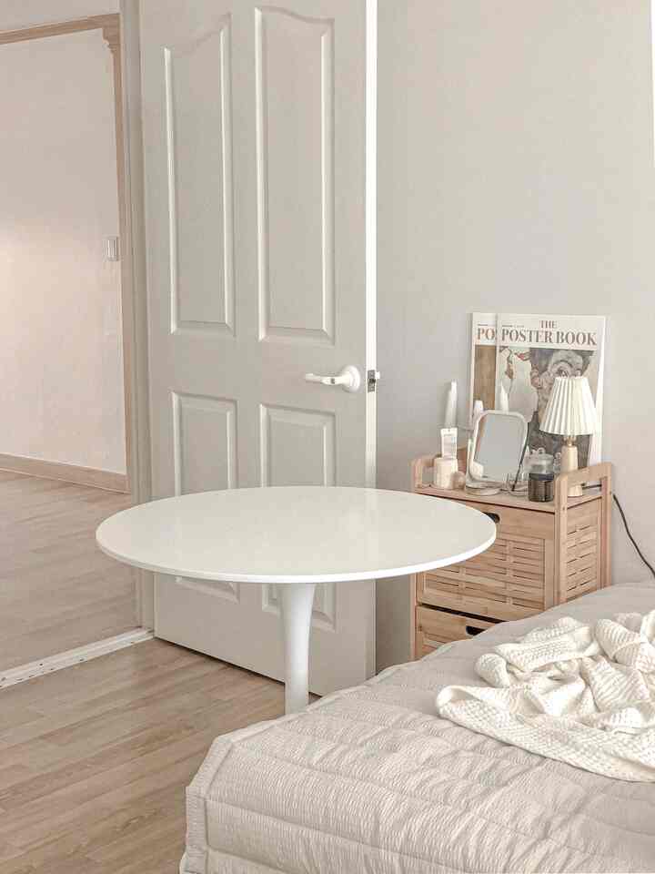 白と木目調が調和する寝室、丸テーブルと木製収納キャビネットが配置された温かみのあるインテリア