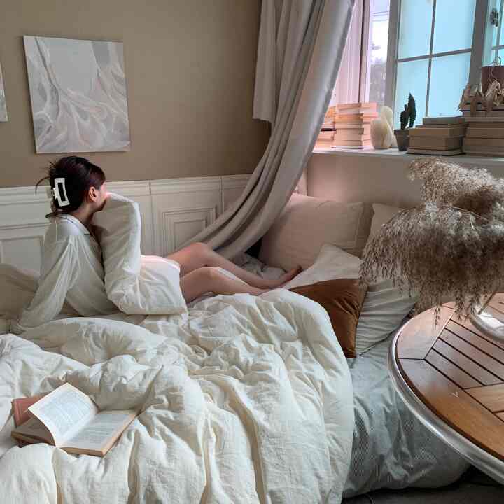 Ivory and beige toned studio apartment bedroom featuring cozy duvet cover, cushions, books, and plants, creating a relaxed atmosphere