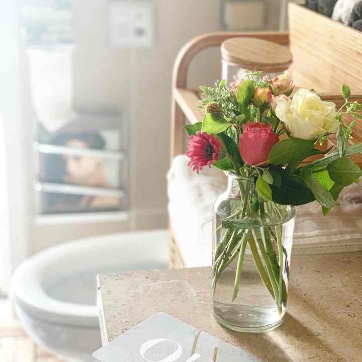 White and wood tone bathroom featuring a glass vase with flowers and storage shelves creating a cozy atmosphere