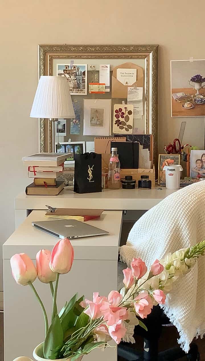 Natural beige-walled home office featuring a white desk, framed wall art, and pink flowers creating a warm atmosphere