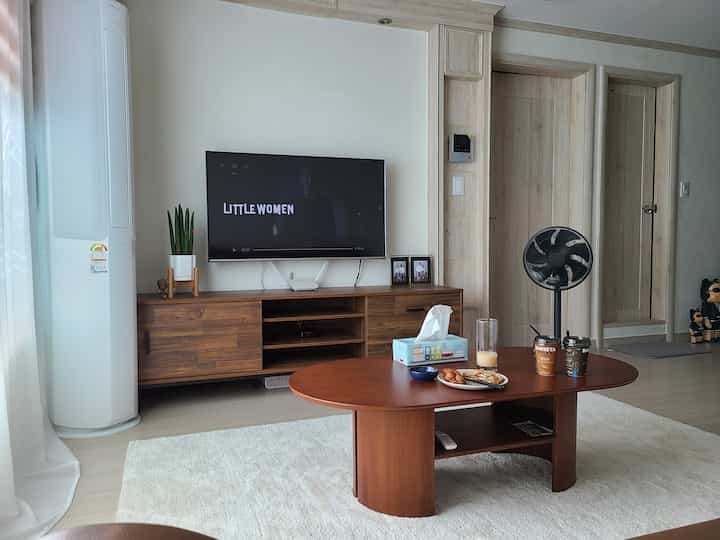 A modern and open living room in wood tones and white, featuring a wooden TV stand and a round wooden coffee table