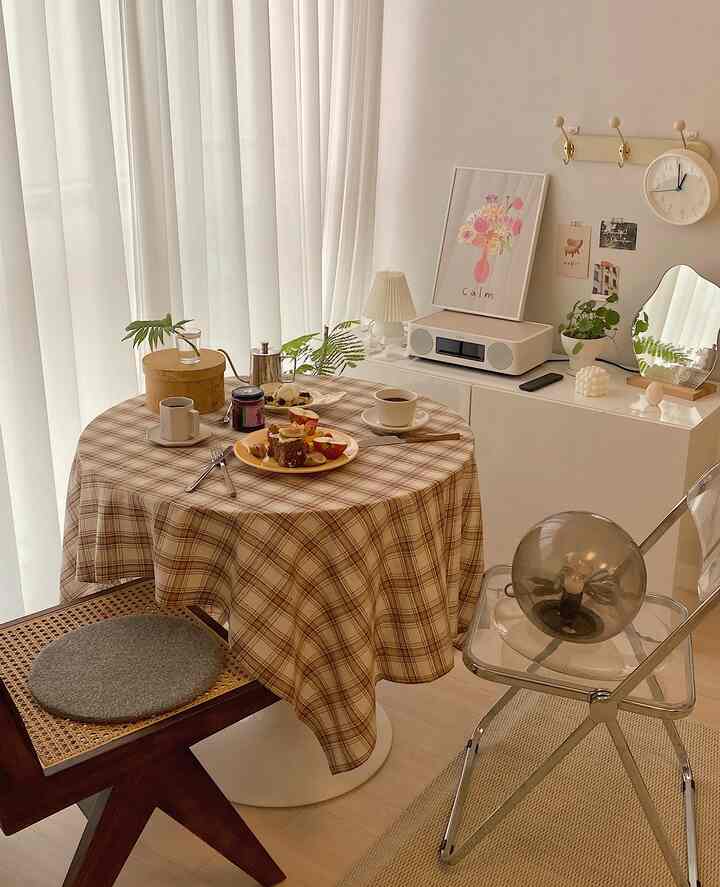 Beige and white toned dining room featuring a round table with plaid tablecloth, coffee cups, chairs, and audio equipment creating a cozy home cafe vibe