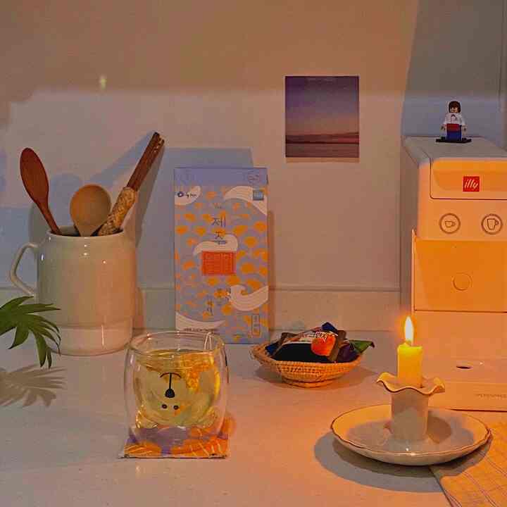 Cozy home cafe kitchen in white with warm gold lighting, featuring Jeju tangerine peel tea, coffee machine, and a lit candle