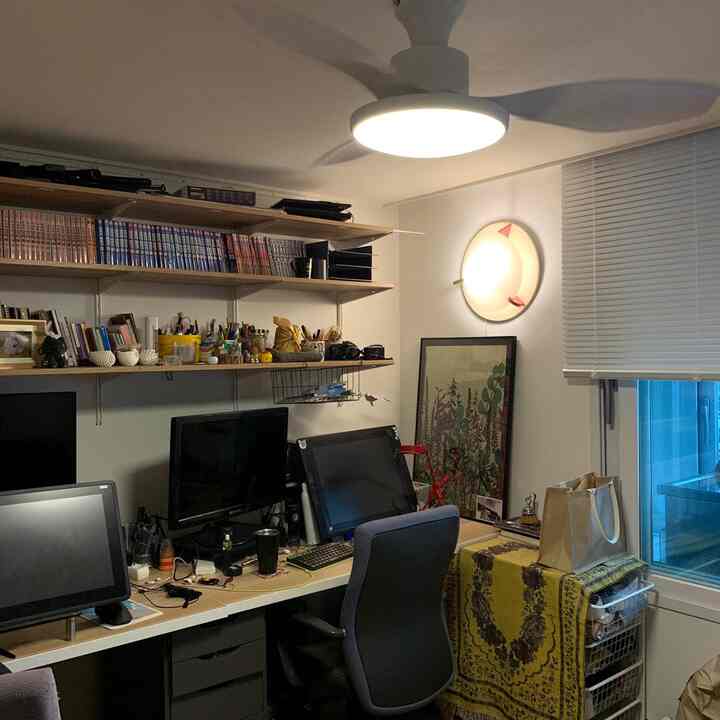 A white and wood-toned workspace featuring multiple monitors and vintage lighting in a practical home office setting