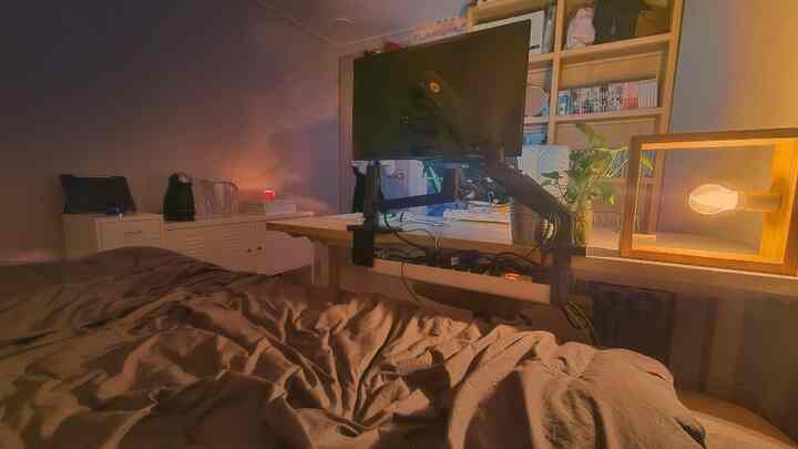 Warm brown-toned small room combining bedroom and workspace, featuring monitor and lift-up bed creating a cozy area
