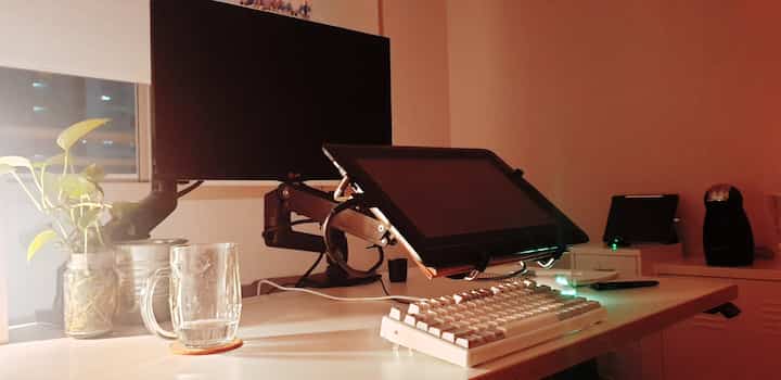 Cozy home office workspace with white desk, monitor arms, and plants under warm lighting