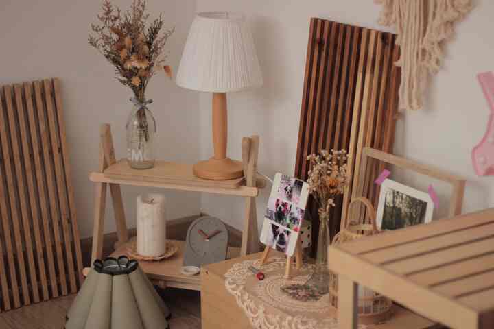 ナチュラルなウッドトーンの落ち着いた空間、折りたたみ棚と卓上時計、ドライフラワーの飾りが調和したミニマルなインテリア