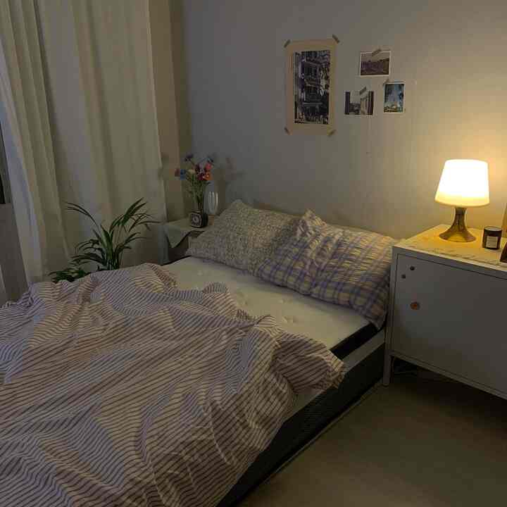 Cozy bedroom with warm lighting and vintage décor, featuring a tidy mattress and striped duvet in a compact space