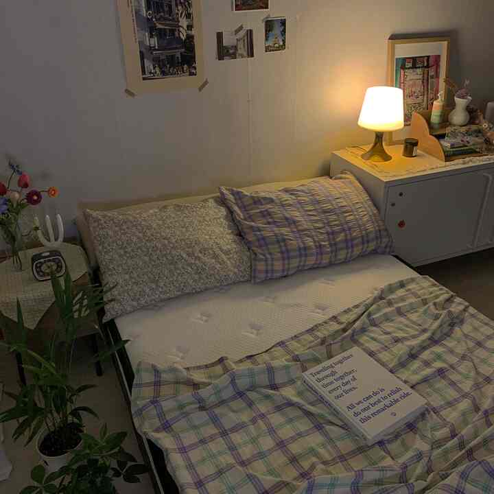 Warm lighting bedroom space featuring mattress, nightstand, and plants arranged for cozy atmosphere