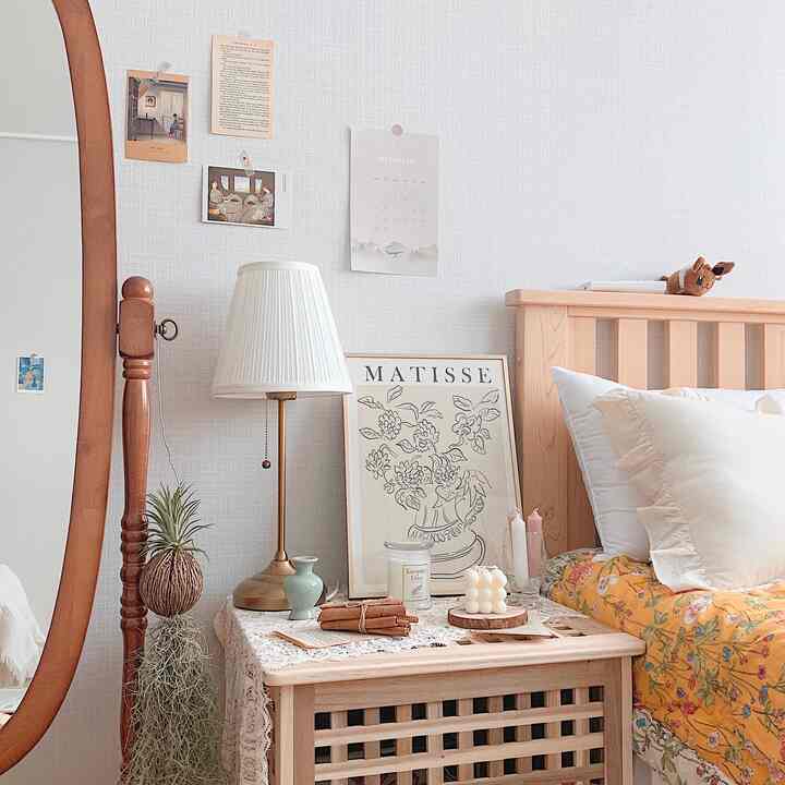 Bright wood-tone bedroom featuring floral bedding, white pillows, table lamp, and framed art creating cozy atmosphere