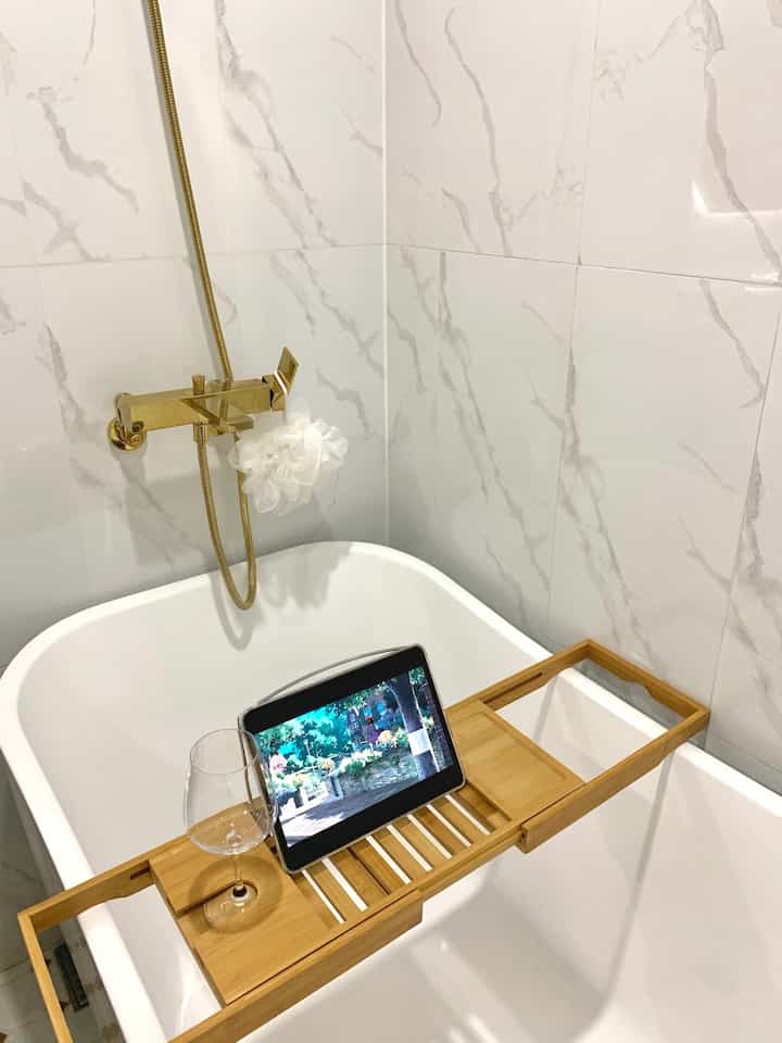 白と木目調のバスルーム、浴槽の上に置かれたトレイとワイングラスが配置された雰囲気のある空間