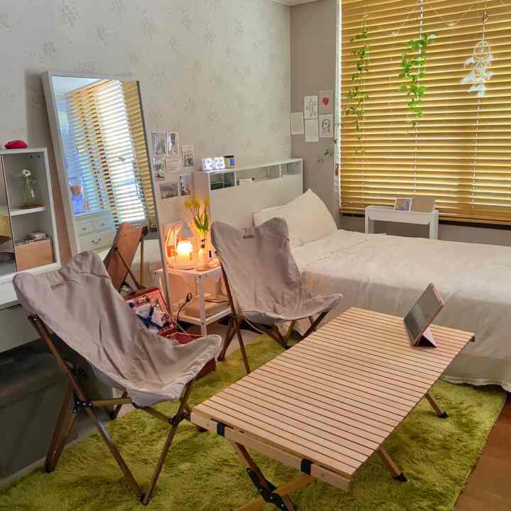 Natural wood tone living room-bedroom space featuring camping chairs and a wood roll table with cozy home camping vibe