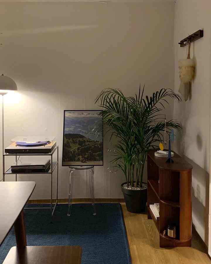 ナチュラルな色調と透明感のあるホームオフィス空間、アレカヤシの観葉植物と透明スツール、木製のサイドボードが配置された落ち着いた雰囲気のインテリア