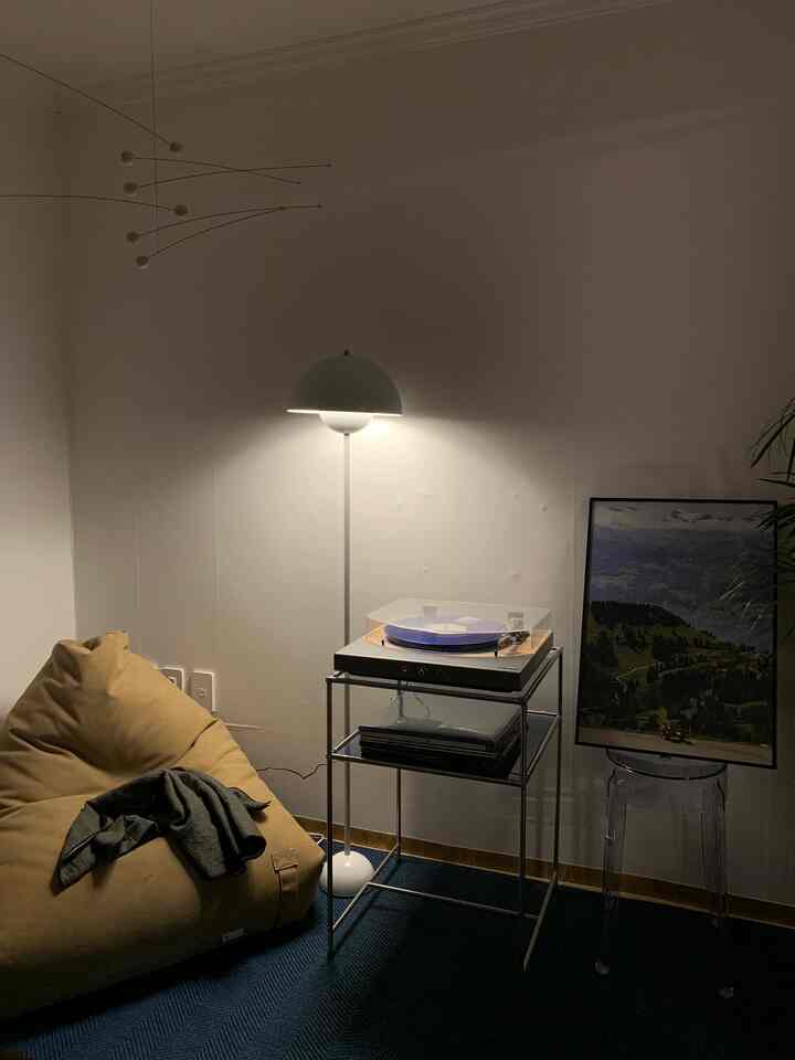 温かみのあるナチュラルカラーのリビング、マスタード色のビーンバッグソファと白いフロアランプ、透明なプラスチックのスツールが配置された雰囲気あるインテリア